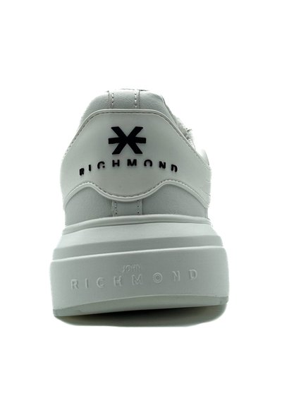 Sneaker bianco con pelle texture, colletto imbottito e una suola piatta spessa. Presenta il logo nero e il nome del marchio sul tallone e sul lato.