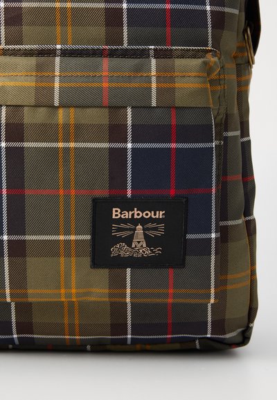Poche avant d'un sac à dos à carreaux verts, bleu marine et rouges avec un patch noir portant le texte "Barbour" et un graphique de phare en beige.