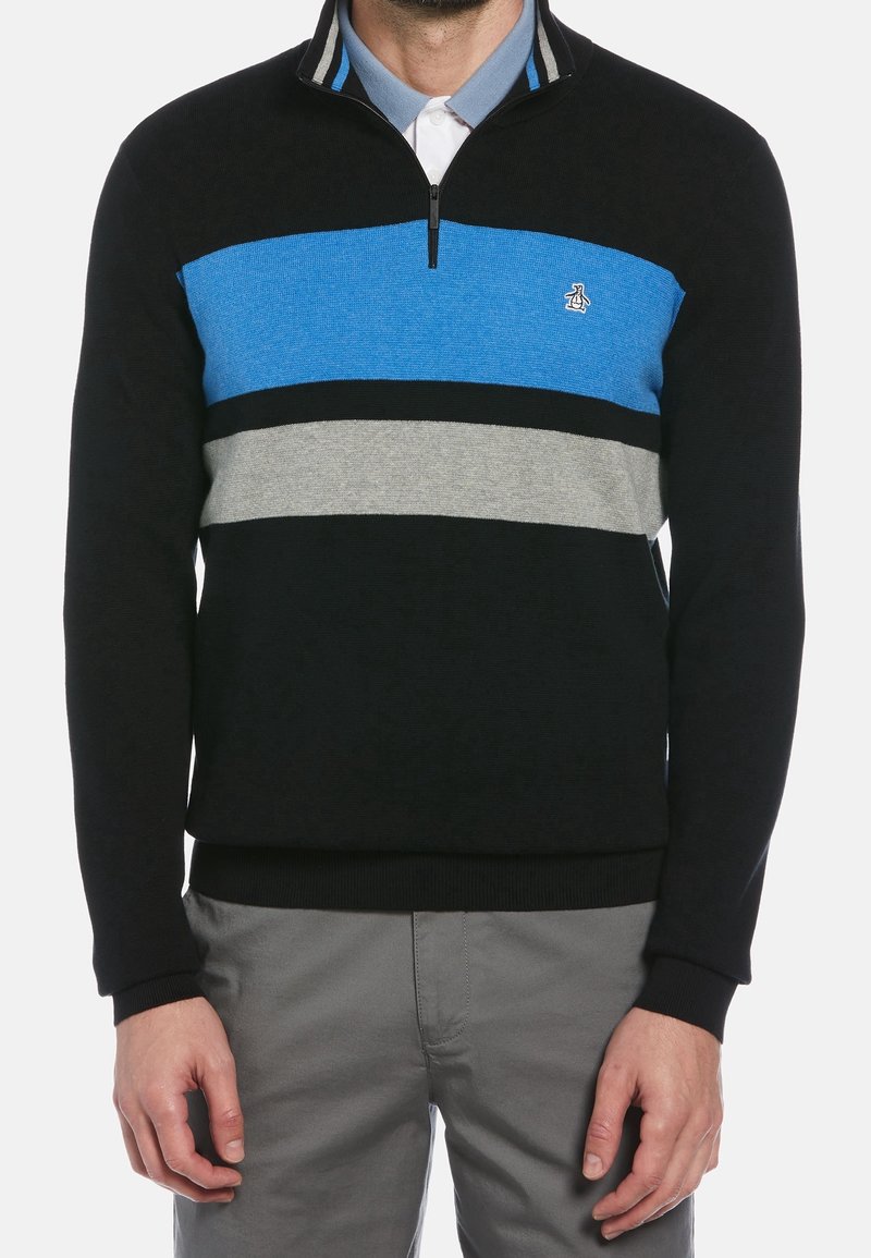 Homme portant un pull noir avec des rayures horizontales bleues et grises et un col à demi-fermeture éclair, assorti d'un pantalon gris.