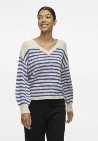 Pull rayé beige et bleu, avec un col en V, une coupe décontractée et des poignets côtelés. Fabriqué en tricot léger.