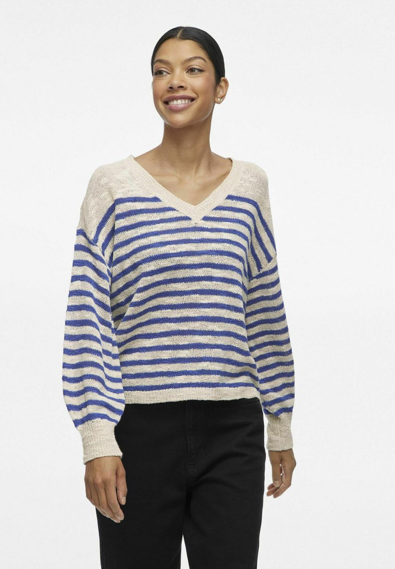 Pull rayé beige et bleu, avec un col en V, une coupe décontractée et des poignets côtelés. Fabriqué en tricot léger.