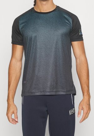Mann trägt ein kurzärmeliges dunkles Gradient-Sportshirt und marineblaue Hosen mit kleinem EA7-Logo am linken Oberschenkel.