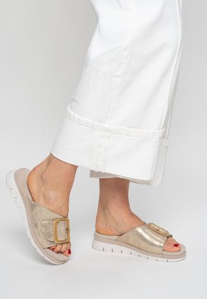 Slide sandals in metallic gold with a wide strap and a large buckle. Textured surface and lightweight white sole with grooves.