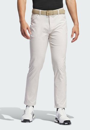 Ljusbeige chinos med en slät textur, rak passform och sidofickor, kombinerade med ett flätat brunt bälte och vita golfsandaler.