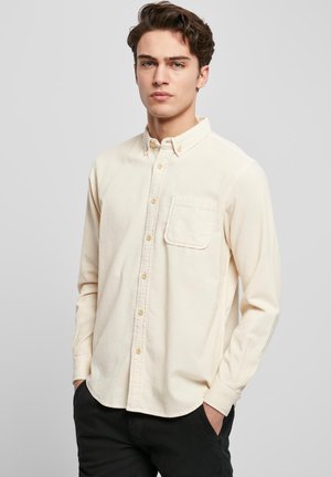 Cream long-sleeve button-up shirt with a chest pocket, featuring a pointed collar and rounded hem. Soft texture and golden buttons.