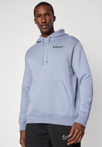 Svetlomodrá mikina s kapucňou a prednou kapsou, s čiernym logom "SPURS" a Nike swoosh. Vyrobená z mäkkej látky, s nastaviteľnými šnúrkami.