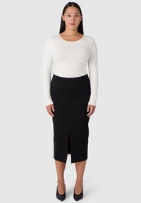 Svart pennkjol med en framficka, tillsammans med en figurnära vit långärmad topp. Slät tygtextur och skräddarsydd silhuett.