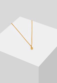 Collier en chaîne dorée présentant un design fin et délicat avec un petit pendentif rond. La chaîne a une texture lisse et un éclat subtil.