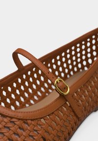 Καφέ επίπεδο δερμάτινο παπούτσι πλεγμένο, με διάτρητες πλευρές και χρυσή αγκράφα στον ιμάντα πάνω από το πέλμα.