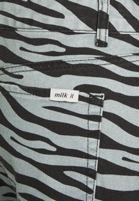 Calças de ganga em azul claro desbotado com riscas de zebra abstratas em preto e um rótulo branco "milk it" no bolso de trás.