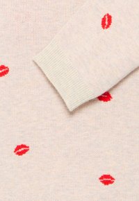 Suéter de punto en beige claro con acentos de estampado de labios rojos, con puños acanalados, textura suave y un diseño casual.