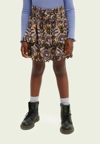 Nederdel med blomstermønster i jordfarver, med flæser og en indsnævret talje, kombineret med sorte militærstøvler og grå sokker.