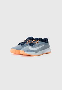 Sportliche Schuhe mit einem hellgrauen Mesh-Obermaterial, marineblauen Akzenten und einer orangefarbenen Gummisohle. Sie verfügen über eine strukturierte Oberfläche und eine verstärkte Zehenpartie.