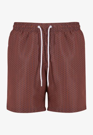 Czerwone kąpielówki w wzory z białym sznurkiem, z czarną naszywką logo. Noszone z czarnymi klapkami na boso.