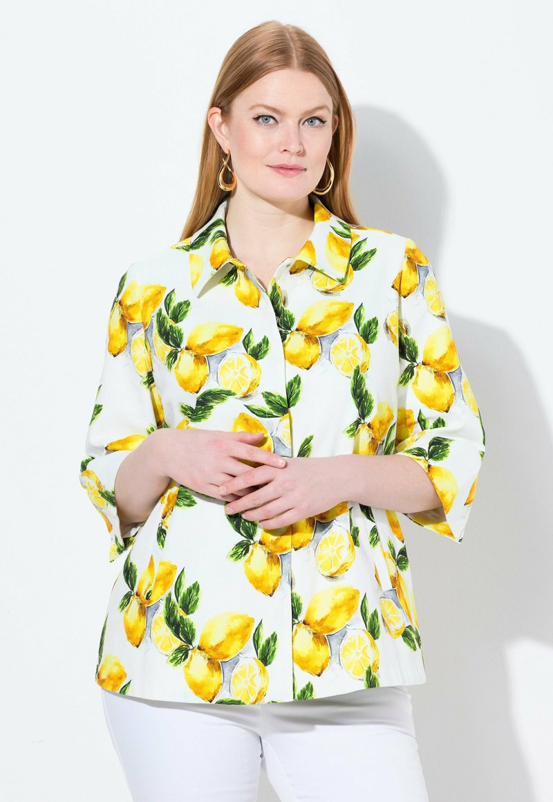 Camicia bianca a maniche lunghe con un vivace motivo di limoni accompagnato da foglie verdi e dettagli gialli. Maniche a tre quarti e un design di vestibilità morbida.