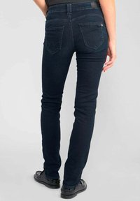Jeans ajustados de color azul oscuro, confeccionados en denim, con una cintura estándar, bolsillos traseros con costuras decorativas y un diseño de corte slim.