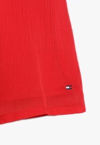 Tissu rouge texturé avec un ourlet droit et une petite étiquette logo multicolore cousue dans le coin inférieur gauche.