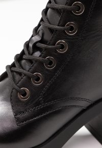 Black leather boot with rounded toe, flat heel, metal eyelets, and black laces. Smooth texture with stitched detailing on the side.