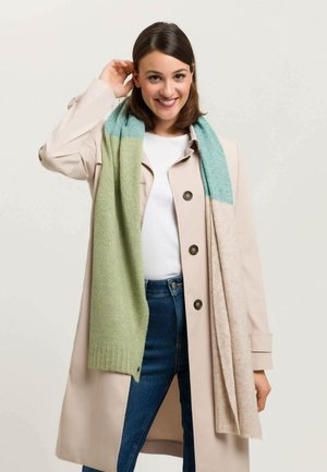 Knit scarf featuring a gradient design in light green and teal, with a soft texture, draped casually over a cream coat.