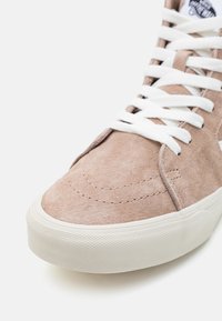 Høye sneakers i lys beige semsket skinn med hvite snører, med en teksturert gummisåle og sømdetaljer på forfoten.