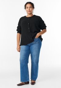 Črn pulover s gumbi iz mehke, teksturirane tkanine, kombiniran z svetlo modrimi širokimi kavbojkami in temnimi balerinkami. Preprost, priložnostni videz.