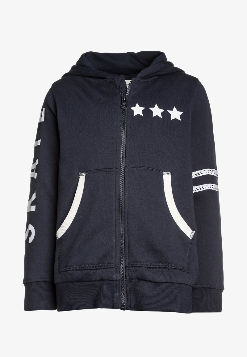 Haut à zip bleu marine avec trois étoiles blanches imprimées au-dessus de la fermeture éclair, présentant des rayures blanches sur les manches et deux poches avant.