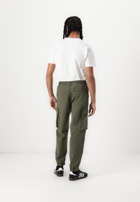 Olivgrüne Cargo-Hosen mit elastischen Bündchen, Seitentaschen und einem Kordelzugbund. Kombiniert mit einem schlichten weißen T-Shirt mit kurzen Ärmeln.