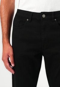 Jean noir avec un design ajusté, doté d'une fermeture à bouton en métal, de passants de ceinture et de poches avant. Texture en denim lisse et durable.