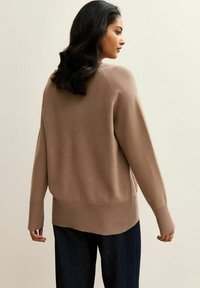 Suéter marrón de tejido de punto suave, corte relajado con puños y dobladillo acanalados, que presenta una abertura lateral y un back ligeramente más largo.
