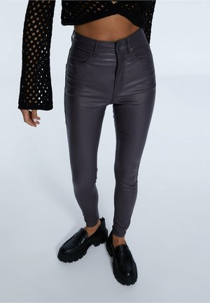 Personne portant un pantalon en cuir slim gris foncé à taille haute, des mocassins noirs épais et un crop top en crochet à manches longues noir.