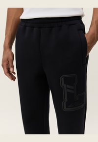 Marineblå sweats med elastisk talje, sidelommer og et stort sort logo på låret. Fremstillet af blødt, tekstureret stof.