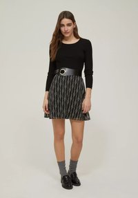 Top nero a righe con maniche lunghe e gonna svasata con un motivo a catena, cinte in vita da una larga cintura nera con hardware dorato.