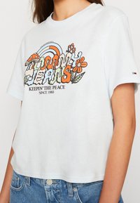 Bílý zkrácený tričko s barevným retro logem Tommy Jeans, houbou, duhou, motýlem, usmívajícím se květinou a textem "Udržujeme mír od roku 1985".