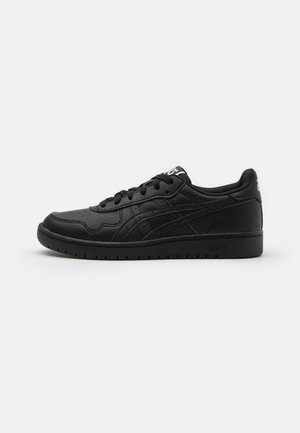 Low-top sort sneaker med snørebånd, teksturerede sidestriber og hvidt logo på tungen, vist på en ensfarvet lys baggrund.