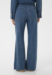 Blue denim wide-leg trousers with a high waist, featuring two back pockets and a relaxed fit. Textured fabric with visible stitching.