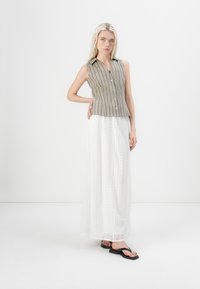 Ärmelloses gestreiftes Oberteil in Oliv und Creme, kombiniert mit einem weißen Spitzen-Maxikleid und schwarzen Flip-Flops. Einfache Knopfdetails am Oberteil.