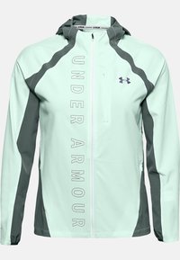 Jasno miętowa kurtka biegowa z ciemnoszarymi akcentami, pełnym zamkiem, kapturem i logo "UNDER ARMOUR" w pionowym tekście na przodzie.