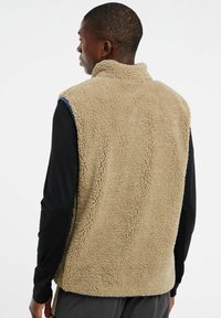 Beige Fleece-Weste mit hohem Kragen, mit strukturierter Oberfläche, ärmellosem Design und kontrastierendem blauen Besatz entlang der Armausschnitte.