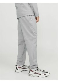 Pantalones deportivos grises hechos de una tela suave, con bolsillos, cinturilla elástica y un corte holgado, combinados con zapatillas deportivas multicolores.