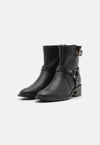 Bottes noires en cuir à cheville avec un bout pointu, dotées d'une sangle à boucle latérale et d'un talon bloc orné d'un accent doré. Texture lisse, design minimaliste.