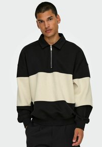 Schwarzer und cremefarbener color-blocked Pullover mit Reißverschluss-Kragen, lockerer Passform, gerippten Bündchen und Saum. Fleece-ähnliche Textur.