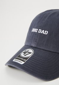 Marineblauwe katoenen pet met geborduurde tekst "DOG DAD" in het wit. Heeft een gebogen klep en een verstelbare band; het label vermeldt "47 CLEAN UP."