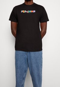 Svart bomull t-shirt med flerfärgad "PALMTREE" text framtill, ihopparad med ljusblå denimjeans.