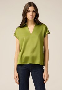 Bluză verde din satin cu guler în V, mâneci scurte și croială lejeră. Designul include o textură netedă, cu un luciu subtil.