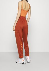 Orange ribbad bodysuit i kombination med höga rostfärgade cargobyxor som har sidofickor och Nike-märke i orange. Vita sneakers fulländar looken.