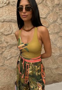 Gelb-grünes, gemustertes Tanktop mit floralem Design, kombiniert mit lockeren, mehrfarbigen Hosen mit tropischen Motiven und einem korallenfarbenen Bund.