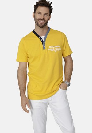 Gelbes T-Shirt mit kurzen Ärmeln und einem grau-blauen Kragen, ausgestattet mit einer Knopfleiste und weißem Text mit der Aufschrift "CHALLENGER WORLD SAILING."