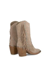 Beżowe zamszowe botki za kostkę z frędzlami, dekoracyjnymi ćwiekami, spiczastym czubkiem i słupkowym obcasem o drewnopodobnym wykończeniu.