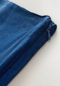 Kék farmer szövetből készült tasak cipzáras záródással, világos felületen, ferde nézetben, a cipzár területére fókuszálva.