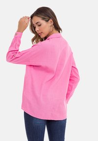 Rosa Leinenhemd mit Kragen, langen Ärmeln und Knopfakzenten an den Bündchen. Lockerer Schnitt mit abgerundetem Saum und weicher Textur.